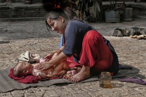 A lato della maestosa Durbar Square di Kathmandu, in un cortile interno, una mamma Newari massaggia amorevolmente il suo piccolo bimbo disteso a terra su un telo, Kathmandu, Nepal 2018.