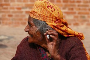 Questa anziana donna Newari, seduta sul lastricato della piazza di Durbar Square di Bhaktapur, si gode la sua sigaretta mentre osserva i nipotini che giocano poco lontano, Nepal 2018.