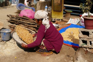 Nel cortile antistante la sua abitazione, questa donna Newari fa saltare il mais per separarlo meglio dalla crusca con movimenti precisi del setaccio che scaglia verso l'alto i chicchi, per poi porli su un telo ad asciugare al sole, villaggio di Khokana, Nepal 2018.