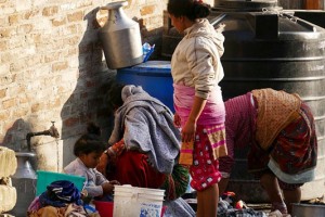 Tre donne Newari fanno il bucato presso una fontana mentre una bambina gioca imitandole, villaggio di Kirtipur, Nepal 2018.