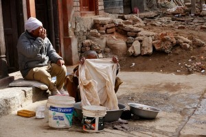 Una anziana coppia Newari sull'uscio della loro abitazione: la donna lava a mano il bucato all'interno di bacinelle in alluminio mentre il marito è alla ricerca di qualche "tesoro" nel naso, villaggio di Khokanà, Nepal 2018.