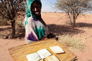 Giovane donna Fulani offre, su un lato della pista sterrata ai rari possibili avventori, alcuni panetti di formaggio distesi su una stuoia in canne intrecciate. Deserto del Sahara, Regione dell'Air, Niger 2020