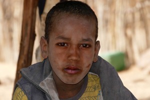 Lo sguardo della speranza. Bambino nomade Peul. Crescono in fretta i bambini della sua età. Lui si chiama Ahmed, ha 11 anni e dall'età di 7 conduce le mandrie degli zebù insieme al padre alla ricerca dei rari pascoli. Si sono accampati con le loro tende in questo "Kori", un letto asciutto di un antico fiume ormai in secca. Massiccio montuoso dell'Air, Niger 2020