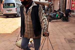 Un anziano Sherpa porta con un bilancere sorretto da una grande canna di bambù posta sulle spalle alcuni oggetti particolarmente pesanti, Bhaktapur, Nepal 2018