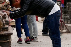 Lungo la spianata del complesso dove sorge il Tempio buddhista di Swayambhunath; un devoto, appartenente all'etnia degli Sherpa, esegue il rituale della "Puja", pregando e inchinandosi dinanzi al Tempio di Hariti, la Dea del vaiolo. Questa pagoda dorata contiene una splendida statua di Hariti: la Dea Hindu che veglia anche sulla fertilità, ciò a dimostrazione delle profonde affinità e corrispondenze, oltre all'armonia ed alla tolleranza che in Nepal unisce e contraddistingue il buddhismo e l'hinduismo. Kathmandu, Nepal 2018.