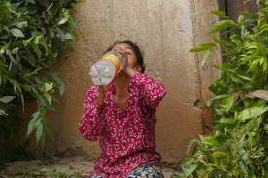 Una delle donne Sherpa che ha affrontato la ripida salita dalla campagna al villaggio con il peso sulla schiena del foraggio destinato agli animali, si rifocilla seduta a terra bevendo acqua, Villaggio di Khokanà, Nepal 2018.