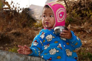 Un bambino nepalese di etnia Tamang si gusta il riso contenuto nella ciotolina di metallo mentre resta appoggiato ad un muretto poco distante dall'abitazione della sua famiglia (il nome Tamang in tibetano significa "mercanti di cavalli": anticamente gli antenati di questo bimbo sono entrati in contatto con le popolazioni locali per fini commerciali, sino a sedentarizzarsi nei territori dell'attuale Nepal; attualmente svolgono frequentemente l'attività di portatori, al pari degli Sherpa, basandosi sulla loro profonda conoscenza delle montagne facenti parte del Massiccio montuoso dell'Himalaya; il Buddhismo è molto diffuso, anche se spesso contaminato con elementi dell'antica religione "Bon", il Lama cioè il sacerdote, ha un ruolo fondamentale all'interno della comunità, celebrando matrimoni e funerali; numerosi clan Tamang vietano il matrimonio interetnico mentre altri lo consentono limitatamente ai membri delle etnie Gurung, Magar, Newari e Chhetri; è comunque proibito il matrimonio all'interno dello stesso clan). Nepal 2018.