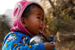 Questa bambina Tamang si aiuta con le dita a mangiare gli ultimi chicchi di riso dalla sua ciotola (il nome Tamang in tibetano significa "mercanti di cavalli": anticamente gli antenati di questo bimbo sono entrati in contatto con le popolazioni locali per fini commerciali, sino a sedentarizzarsi nei territori dell'attuale Nepal; attualmente svolgono frequentemente l'attività di portatori al pari degli Sherpa basandosi sulla loro profonda conoscenza delle montagne facenti parte del Massiccio montuoso dell'Himalaya; il Buddhismo è molto diffuso, anche se spesso contaminato con elementi dell'antica religione "Bon"; il Lama, cioè il sacerdote, ha un ruolo fondamentale all'interno della comunità celebrando matrimoni e funerali; numerosi clan Tamang vietano il matrimonio interetnico mentre altri lo consentono limitatamente ai membri delle etnie Gurung, Magar, Newari e Chhetri; è comunque proibito il matrimonio all'interno dello stesso clan). Nepal 2018.