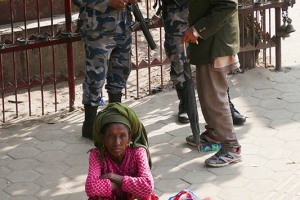 Nel villaggio di Panauti una donna Tamang su un banchetto improvvisato vende la frutta che lei stessa ha raccolto dall'albero, alle sue spalle un anziano uomo Newari dialoga con due militari di ronda, Nepal 2018.