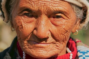 Primo piano di una anziana donna nepalese appartenente all'etnia Thakali indossa i vestiti tradizionali: il suo viso bruciato dal sole e le sue mani non certamente appena uscite dalla manicure, testimoniano il duro lavoro svolto durante la sua vita nei campi. I Thakali sono originari della Valla del Kali Gandaki, nel Nepal centrale, ed un tempo svolgevano un ruolo importante nel commercio del sale tra il subcontinente indiano ed il Tibet, ora li si incontra prevalentemente lungo la catena montuosa dell'Annapurna. In origine professavano la fede religiosa buddhista ma negli ultimi anni la maggioranza ha abbracciato in modo pragmatico l'hinduismo. Dintorni del villaggio di Pachabhaiya, Nepal 2018.