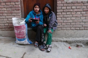 Questi due bambini nepalesi appartenenti all'etnia Thakali giocano con il telefono durante una pausa dal lavoro: il loro sguardo alla mia vista è, rispettivamente, di sorpresa e di complicità. Il sacco pieno di cemmento testimonia il loro sforzo di piccoli manovali. Pokhara, Nepal 2018.