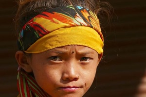 Una bambina nepalese di etnia Tharu presenta ben visibile al centro della fronte un segno nero tondo, cosiddetto "tilaka", ricavato dalle ceneri utilizzate in qualche rituale religioso, che è il segno distintivo dei seguaci del Dio Shiva. Il credo religioso dei Tharu è, in larga parte, animista (contempla il culto degli spiriti della foresta e delle divinità ancestrali), ma la dottrina hindu sta esercitando un'influenza ed una diffusione crescente ed inarrestabile. Villaggio di Kasara, Chitwan National Park, Nepal 2018.