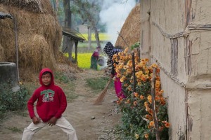 Un bambino appartenente all'etnia Tharu mi accoglie compiendo alcuni passi di danza, mentre la sorella pulisce il cortile e la mamma bada al fuoco: il suo neme è Laxu ed ha 12 anni, Villaggio di Bacchauli, Nepal 2018.