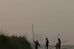 Quattro pescatori Tharu avanzano con le loro barche spingendosi sul fondo del fiume Rapti con i loro lunghi bastoni alle prime luci dell'alba, Chitwan National Park, Nepal 2018.