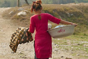 Sulla bacinella in alluminio che contiene i panni appena lavati, vi è un'iscrizione in lingua sanscrita che riproduce il nome della ragazza che la trasporta: il suo nome è "Savedi", dintorni del villaggio di Harnari, Chitwan National Park, Nepal 2018.
