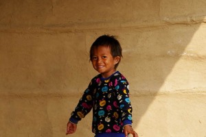 Una bambina Tharu mi sorride accanto alla sua capanna di fango nel villaggio di Harnari, Chitwan National Park, Nepal 2018.