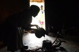 Interno in controluce di una capanna del popolo Venda: una donna versa dell'acqua su una pentola posta sul fuoco, Provincia del Limpopo, Sud Africa 2012