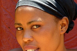 Giovane e affascinante donna appartenente al Popolo Xhosa, il secondo maggior gruppo etnico del Sud Africa dopo gli Zulu. Lo stesso Nelson Mandela era uno Xhosa, il "Popolo rosso" come solitamente viene definito a causa degli abiti di colore rosso che indossano prevalentemente. L'abbigliamento per loro ha un "codice" abbastanza complesso: il rosso e l'arancione sono i colori base che vengono solitamente utilizzati, ma il loro modo di vestire può cambiare in base alla posizione sociale ed in base alla fase della loro vita. Le donne sposate, ad esempio, indossano una specie di turbante intrecciato colorato, con stili differenti a seconda di chi lo indossa: una ragazza appena sposata avrà un copricapo differente da quello di una donna che ha messo al mondo il primo figlio. Gli abiti vengono decorati ed impreziositi da complesse lavorazioni realizzate con perline colorate, perle di vetro, semi, gusci ed altri materiali naturali che rendono questi capi dei veri e propri capolavori.Villaggio Lesedi, Sud Africa 2012
