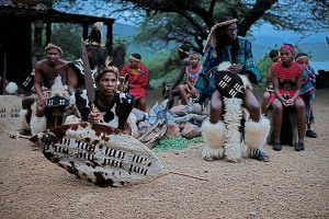 I guerrieri Zulu, accompagnati da giovani ragazze, si apprestano ad iniziare le danze tribali tradizionali, Villaggio Shakaland, Provincia del KwaZulu-Natal, Sud Africa 2012