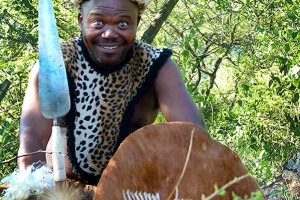 Guerriero Zulu con il tipico copricapo a fascia ("Umqhele") ricavato dalla pelle dell'Impala e realizzato con un tubo di pelliccia imbottito con sterco di vacca o fibre vegetali, indossa inoltre le piume di struzzo ("Upaphe") e stringe tra le sue mani la corta lancia con la punta larga come una sciabola ("Assegai") ed il grande scudo rivestito di pelle di vacca ("Isihlangu"), il torace è parzialmente coperto da una casacca di pelle di leopardo, Villaggio Shakaland, Sud Africa 2012