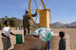 Bambine bevono direttamente dal pozzo, posto al centro del letto asciutto di un fiume, che aspira acqua tramite il movimento manuale ( in senso orario) di una grande ruota,  Villaggio di Timia, Regione dell'Air, Niger 2020