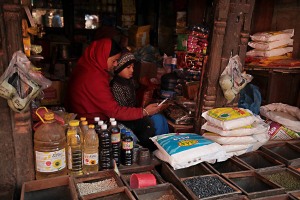 Nella piazza del mercato di Lagankhel, adiacente alla fermata degli autobus, si trovano numerose botteghe che offrono qualsiasi prodotto alimentare e non: una donna nepalese appartenente alla casta dei "Vaisya" (commercianti) mostra al suo bambino qualcosa sul cellulare, Patan, Nepal 2018