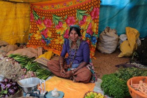 Gautami, una donna appartenente all'etnia nomade Banjara vende i suoi prodotti agricoli nel mercato di Saundatti in occasione dei festeggiamenti dedicati alla Dea Yallamma: questa tribù transumante che ha uno stile di vita errante viene considerata diretta discendente degli antenati indiani dei Rom europei. Da notare il vistoso abbigliamento tradizionale, le numerose collane ed i tradizionali orecchini di varia fattura. Regione del Karnataka, India 2015.