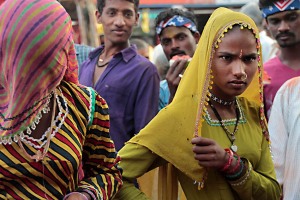 Nella confusione che regna all'interno del mercato di Saundatti, queste due ragazze Hindu dimostrano la loro contrarietà nell'essere fotografate: una si copre il volto e l'altra guarda con ostilità verso l'obiettivo, mentre alle loro spalle due ragazzi si godono la scena divertendosi. Regione del Karnataka, India 2015.