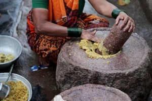 Nel retrobottega di un banco che vende cibo da strada ai clienti del mercato di Saundatti, una anziana donna Hindu di nome Visala macina su una ruota di pietra (simile ad un grosso mortaio) con l'aiuto del pestello i legumi che verranno impiegati nei diversi piatti proposti agli avventori.Regione del Karnataka, India 2015.