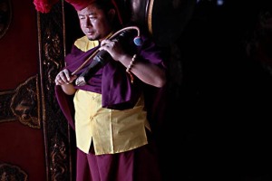 All'ingresso del Guru Lhakhang Monastery, un monaco con il suo tamburo attende i compagni per iniziare la cerimonia Chakra Darma, dintorni dello Stupa di Bodhnath, Kathmandu, Nepal 2018