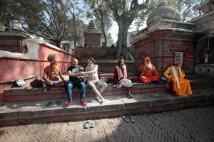 Un gruppo di Sadhu (i santoni indiani), seduti sulle scalinate in pietra che circondano il complesso sacro del Tempio di Pashupatinath, hanno appena "acchialappato" un turista occidentale a cui chiedono offerte in denaro per scattare le fotografie e propongono bracciali e rosari realizzati con i semi di "Rudraksha", Kathmandu, Nepal 2018.