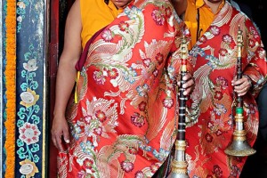 All'ingresso del Guru Lhakhang Monastery di Bodhnath, alcuni monaci tibetani si apprestano a suonare con i loro clarinetti, indossando i loro caratteristici cappelli rossi da cerimonia e sontuose vesti, Nepal 2018