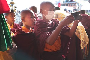 Durante il concerto esterno al Monastero, questo giovane novizio filma con il cellulare i monaci che suonano tamburi e clarinetti durante la Cerimonia del Chakra Darma, mentre il suo compagno osserva il display con attenzione, Guru Lhakhang Monastery di Bodhnath, Nepal 2018