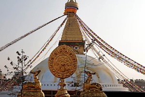 Dalla balconata del Guru Lhakhang Monastery si può ammirare lo Stupa Bodhnath (il più grande di tutta l'Asia) e sul davanzale, in primo piano, si possono contemplare queste notevoli sculture in metallo ricoperte di lamina d'oro riproducenti due gazzelle (simbolo di pacificità e di quiescenza yogica) e la Ruota del Dharma (in sanscrito "Cakra") che si compone di un mozzo centrale e di 8 o più raggi e di un cerchione esterno. Nella cultura Buddhista la ruota è strettamente associata al concetto della Ruota del Dharma messa in moto da Buddha durante la prima esposizione pubblica della sua dottrina a Sarnath presso Benares (l'attuale Varanasi) nel Parco delle Gazzelle. Secondo i tre addestramenti della pratica buddhista, il mozzo rappresenta l'addestramento alla disciplina morale che rende stabile la mente; i raggi rappresentano la comprensione della vacuità di tutti i fenomeni, che permette di eliminare alla radice la nostra ignoranza; il cerchione esterno, infine, identifica la concentrazione che permette di tenere salda la pratica della dottrina buddhista. In particolare la Ruota del Dharma simboleggia l'insegnamento buddhista nella sua globalità e ci ricorda che il Dharma abbraccia tutte le cose, non ha nè inizio nè fine, è in movimento e nello stesso tempo immobile. Nepal 2018