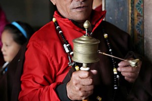 Un fedele buddhista impugna una Ruota delle preghiere ("Chokhor" in tibetano), uno strumento di preghiera per la crescita spirituale e la guarigione.Questo è un modello portatile: è composto da una ruota cilindrica con un coperchio removibile che nasconde al suo interno una cavità dentro cui è arrotolata una pergamena di riso molto lunga e sottile sulla quale è stato trascritto (ripetendolo innumerevoli volte) il mantra "Om Mani Padme Hung" utilizzando i caratteri tibetani. Il mantra è impresso a rilievo anche sulla parte esterna del cilindro che è agganciata ad una maniglia in legno tramite un asso di metallo. Un perno di piombo con una catena è attaccato alla ruota per facilitarne la rotazione. Quando la ruota gira, la preghiera in essa contenuta vola nell'aria e il vento la trasporta in tutto il mondo. Questa pratica religiosa permette di accumulare meriti e sostituire la negatività con nuovi effetti positivi, dando vita ad un buon Karma. Guru Lhakhang Monastery di Bodhnath, Nepal 2018