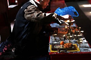 Il custode di un tempio buddhista prepara, nel silenzio della sala di preghiera completamente vuota, i portacandele in ottone che verranno utilizzati per la "Puja" (il rito della preghiera che si esprime attraverso l'adorazione nei confronti della Divinità con offerte, canti e preghiere); il termine Puja è composta dalle sillabe "pa" (peccato) e da "ja" (vittoria), pertanto il suo significato può sintetizzarsi in "ciò che sconfigge il peccato". Santuario dedicato a Saraswati, la Dea della Sapienza, dintorni dello Stupa di Swayambhunath, Nepal 2018