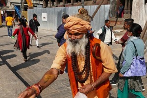 Un Sadhu (asceta hinduista considerato uomo santo: rinuncia ai beni terreni ed alla vita sociale, dedicando l'esistenza alla meditazione ed all'elevazione spirituale. Non ha fissa dimora e si muove da un paese all'altro, da un villaggio all'altro vivendo delle offerte ricevute dai devoti. Spesso si cosparge il corpo ed il volto di cenere, simbolo di morte e di rinascita, porta i capelli lunghi come il Dio Shiva, veste con semplici tuniche e si adorna di collane e di bracciali. Imita Shiva nel fumare la cannabis per "sollevare il velo di Maya" che nasconde l'essenza della realtà) nel cortile antistante il complesso religioso Hindu di Pashupatinath: getta granturco ai piccioni tra il brulicante via via dei pellegrini. Nepal 2018.