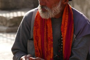 Un sacerdote Hindu ritratto durante una pausa mentre rolla una sigaretta seduto su un muretto del complesso religioso di Pashupatinath, Nepal 2018.