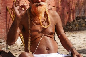 Questo Sadhu si trova nell'area dei santuari shivaiti, lingam e ghat che fanno parte del più ampio ed articolato complesso religioso di Pashupatinath (questo sito è il fulcro dell'energia spirituale hindu, strettamente connesso al Dio Shiva nella sua manifestazione di Pashupati, il signore del bestiame): la sua è una posa standardizzata che assume ogniqualvolta si avvicina un pellegrino, un turista o un fotografo. Kathmandu, Nepal 2018.