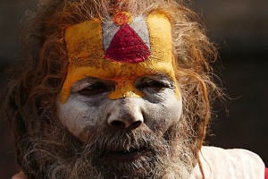 Primo piano di un Sadhu a Pashupatinath: sul suo volto risalta la "Tilaka" tipica dei seguaci di Shiva, chiamata anche "Tripundra", composta da tre strisce di pasta "Vibhuti" (cenere consacrata) di colore bianco con in mezzo un cerchio di pasta di sandalo e di kumkum (polvere di curcuma) arancione, ed infine un triangolo rosso realizzato con la curcuma mescolata con la calce spenta. Kathmandu, Nepal 2018.