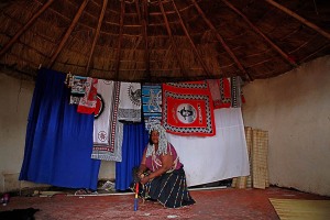 Tipica capanna in un villaggio dello Swaziland, appesi ci sono i ritratti stampati su tela del Re Mswati III, e la donna indossa i vestiti delle feste con una parrucca argentata e impugna i bastoni rituali mentre posa soddisfatta, Swaziland 2012