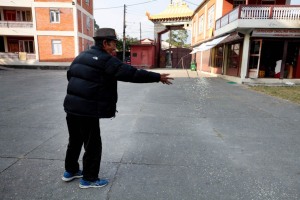 Un anziano rifugiato Tibetano lancia una manciata di riso ai piccioni nel cortile antistante il Gompa di Jangchub Choeling, nel villaggio di Tashi Palkhel: nel Tempio Buddhista vivono circa 200 monaci, Pokhara, Nepal 2018