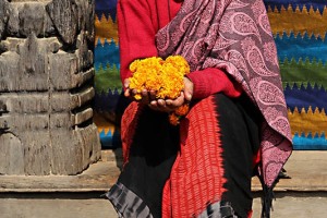 Nello splendido porticato che circonda Durbar Square a Patan, sorretto dalle antiche colonne in legno finemente intarsiato dai mastri scalpellini nepalesi, una anziana donna Newari mi mostra racchiusi tra le sue mani i fiori che utilizzano per realizzare le corone dalle vivaci tonalità, Nepal 2018