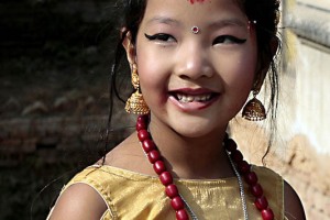 Questa bambina vestita a festa che indossa gli orecchini e monili vari (di nome Bineta) ha appena partecipato ad una cerimonia molto particolare. Si tratta di un matrimonio di "gruppo" in cui centinaia di bambine Hindu e Buddhiste celebrano un matrimonio atipico con un "Bael" un particolare albero da frutto. Secondo questa pratica, prima di raggiungere la pubertà, le bambine devono essere sposate ad un albero di Bael, il cui frutto prende il nome di "Aegle". Questo rito si chiama "Ehi" nella lingua locale newari e coinvolge le ragazzine tra i 5 ed i 12 anni. In genere la cerimonia dura due giorni: inizia con i rituali di purificazione e si conclude con il "Kanyadan", il momento cruciale in cui il padre "dona" la figlia. Nella cultura newari si crede che i genitori possano conquistarsi un posto in cielo sposando le loro figlie prima di avere le mestruazioni. Secondo la tradizione, il frutto ("Aegle") rappresenta lo sposo (simboleggia l'eterno scapolo Kumar, figlio del Dio Hindu Shiva) ed il matrimonio propiziatorio garantisce alla ragazza di diventare e rimanere fertile. Il frutto prescelto deve essere maturo e succoso e non deve riportare alcun danno. Se risultasse ammaccato, la sposa sarà destinata ad avere un marito brutto ed infedele. In realtà, la ragione più importante alla base di questa pratica, consiste nella credenza che la giovane sposandosi con Kuma, rimarrà pura e casta e non potrà essere considerata vedova anche nel caso che il "vero" marito dovesse venir meno, poichè sarà già sposata con una Divinità. Patan, Nepal 2018.