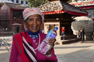 Questa simpatica e sorridente donna Tamang indossa bracciali ed orecchini da naso tradizionali, mostrando con orgoglio la sua bottiglia di acqua potabile appena acquistata al centro della piazza principale di Patan, Nepal 2018.