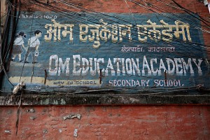 Un cartello stradale dipinto a mano indica la strada per giungere ad una scuola secondaria, raffigurando due bambini che si stringono la mano, Kathmandu, Nepal 2018