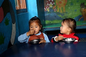 Due bambine nepalesi, rispettivamente appartenenti l'una alla casta dei Brahmini dell'etnia Brahman e l'altra alla casta Kshatriya dell'etnia Chhetri, pranzano mangiando dalle loro ciotole il riso nella mensa della Shree Bal Bikosh Basic School nel quartiere di Cheetrapati a Kathmamdu; la bambina sulla sinistra si chiama "Aishwarya", che significa Principessa, mentre quella sulla destra si chiama "Chandra", che significa Luna. Nepal 2018