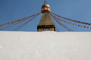 Lo Stupa bianco di Bodhnath nella Valle di Kathmandu con i quattro volti del Buddha che rivolgono lo sguardo sulla Valle verso i 4 punti cardinali: la cupola bianca rappresenta la Terra, l'elemento a 13 livelli simile ad una torre sulla sommità simboleggia i 13 stadi che occorre percorrere per raggiungere il Nirvana, la decorazione posta sotto gli occhi del Buddha simile ad un naso in realtà riproduce la scritta "ek" che corrisponde al numero 1 , cioè l'unità, mentre il terzo occhio al di sopra rappresenta la capacità di intuizione del Buddha. Sopra lo Stupa sono appese migliaia di bandierine di preghiera che riproducono mantra che si narra vengano portati in cielo dal Cavallo del Vento. Alla base dello Stupa centrale sono poste le ruote di preghiera che hanno inciso il sacro mantra "Om mani padme hum" (saluto il gioiello nel loto) e vengono fatte ruotare dai pellegrini nel passaggio (esclusivamente in senso orario) del loro cammino rituale. Kathmandu, Nepal 2018
