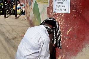 Un uomo "Vaisya" (appartenente alla casta dei commercianti ed agricoltori) prega seduto su uno sgabello con la testa appoggiata contro il muro, Kathmandu, Nepal 2018
