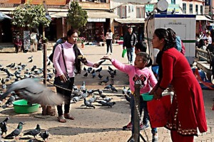 Nel piazzale antistante Bodhnath, lo Stupa più grande di tutta l'Asia, una bambina gioca con i piccioni lanciando loro granaglie, dintorni di Kathmandu, Nepal 2018